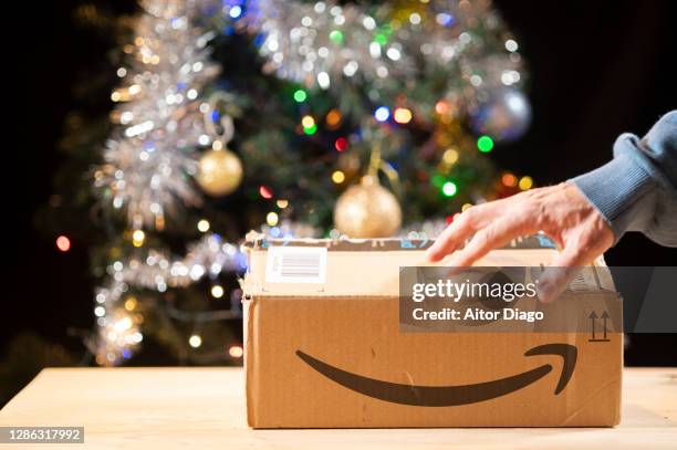 person opening a package in front of a christmas tree. - amazon boxes stock pictures, royalty-free photos & images