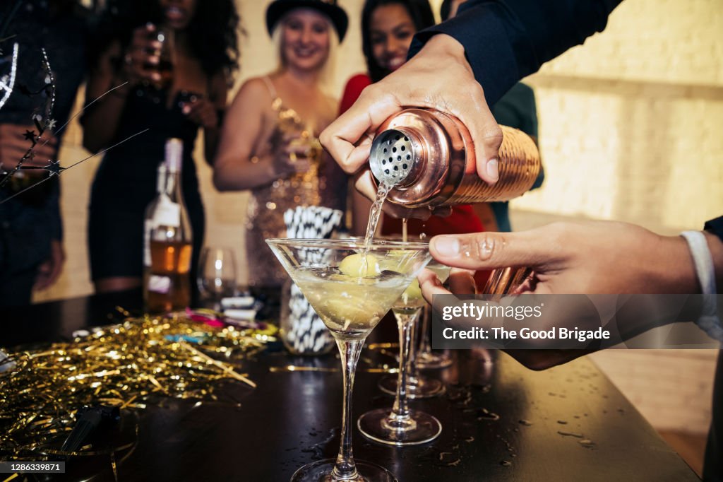 Close-up of hands pouring drink in martini glass at party