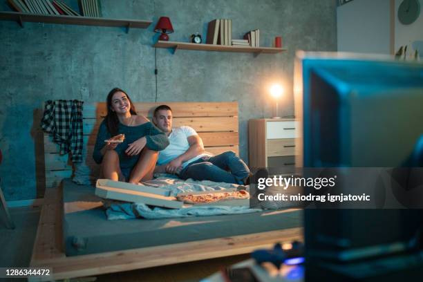 jeune femme mangeant la pizza tout en regardant la tv avec le petit ami la nuit - couple watching tv photos et images de collection