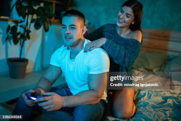 young woman massaging her boyfriend while he's playing video games in bedroom at night - girlfriend massage stock pictures, royalty-free photos & images