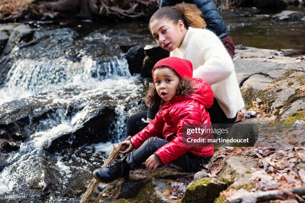 Mixed-race sisters relaxing on river side in autumn nature.