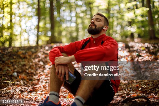 Portret van ontspannen jonge mens met bluetoothhoofdtelefoons in bos Portret van ontspannen jonge mens met bluetoothhoofdtelefoons in bos