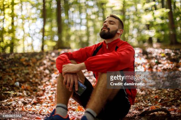 portrait of relaxed young man with bluetooth headphones in forest - resting imagens e fotografias de stock