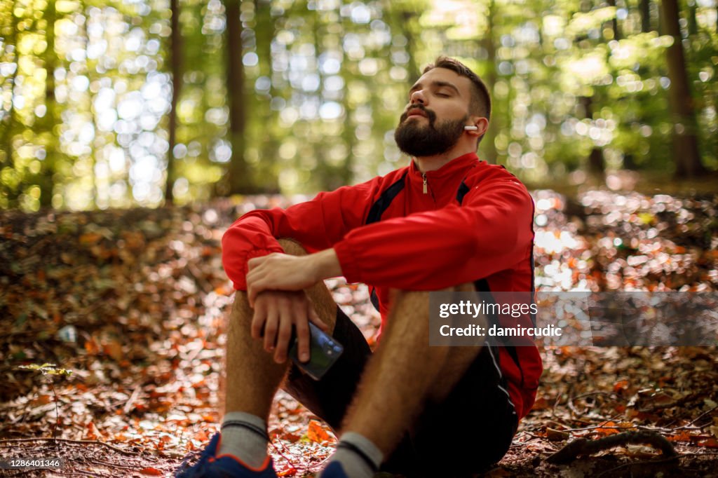 Porträtt av avslappnad ung man med bluetooth hörlurar i skog