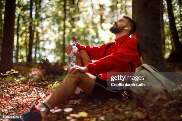 portrait of relaxed young man with bluetooth headphones in forest - exhaling stock pictures, royalty-free photos & images