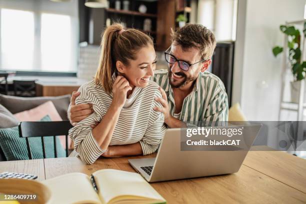 happy couple using laptop at home - young couple laptop stock pictures, royalty-free photos & images