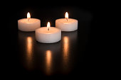 Three white burning tea lights with their reflection on a black background