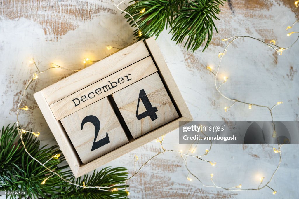Wooden block calendar for Christmas Eve with fairy lights and fir branches