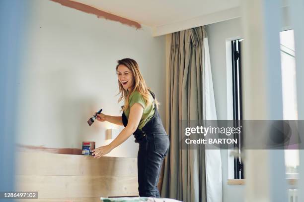 young woman laughs whilst painting bedroom wall - decorar fotografías e imágenes de stock