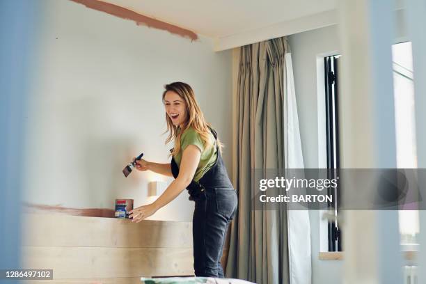 young woman laughs whilst painting bedroom wall - dipinto foto e immagini stock