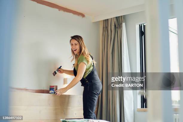 young woman laughs whilst painting bedroom wall - bedroom photos ストックフォトと画像