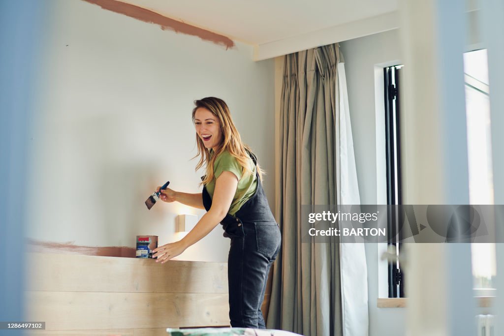 Young Woman laughs whilst painting bedroom wall