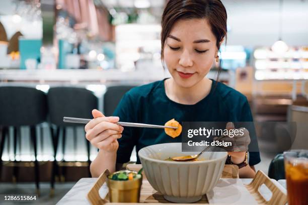 young asian woman eating freshly served authentic thai food, seafood tom yum goong noodles (spicy prawn soup with seafood and noodles). with a refreshing and healthy green salad and iced tea in a thai restaurant. an iconic taste of local thai cuisine - female eating chili bildbanksfoton och bilder