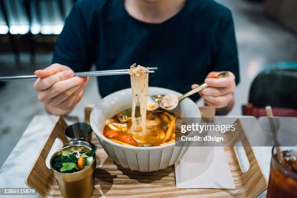 close up of young asian woman eating freshly served authentic thai food, seafood tom yum goong noodles (spicy prawn soup with seafood and noodles). with a refreshing and healthy green salad and iced tea in a thai restaurant. an iconic taste of local thai - pho soup stock-fotos und bilder