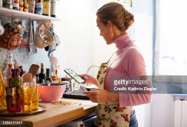 woman making christmas cookies at home, reading recipe on smart phone - baking reading recipe stockfoto's en -beelden