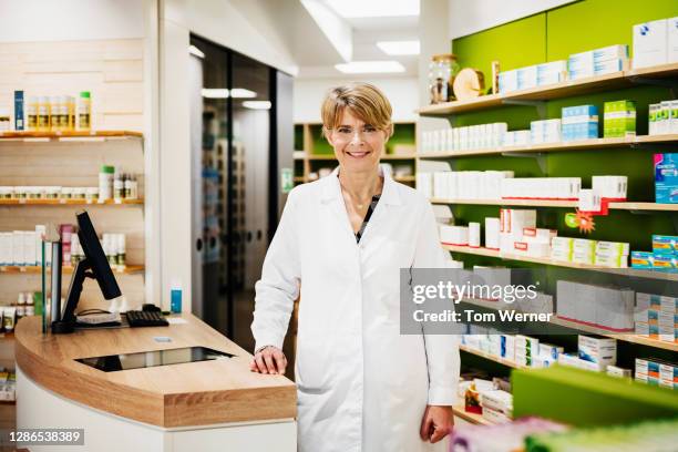 portrait of senior chemist surrounded by medications in pharmacy - apothekerin stock-fotos und bilder