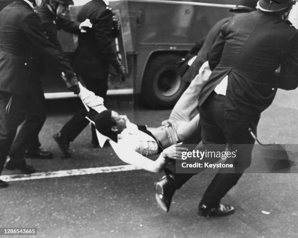 Police officers carrying an arrested man by the arms and legs after violence erupts on the streets of Brixton, London, England, 13th April 1981.