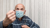 angry aggressive elderly man wearing face mask showing big fist self isolation and coronavirus concept