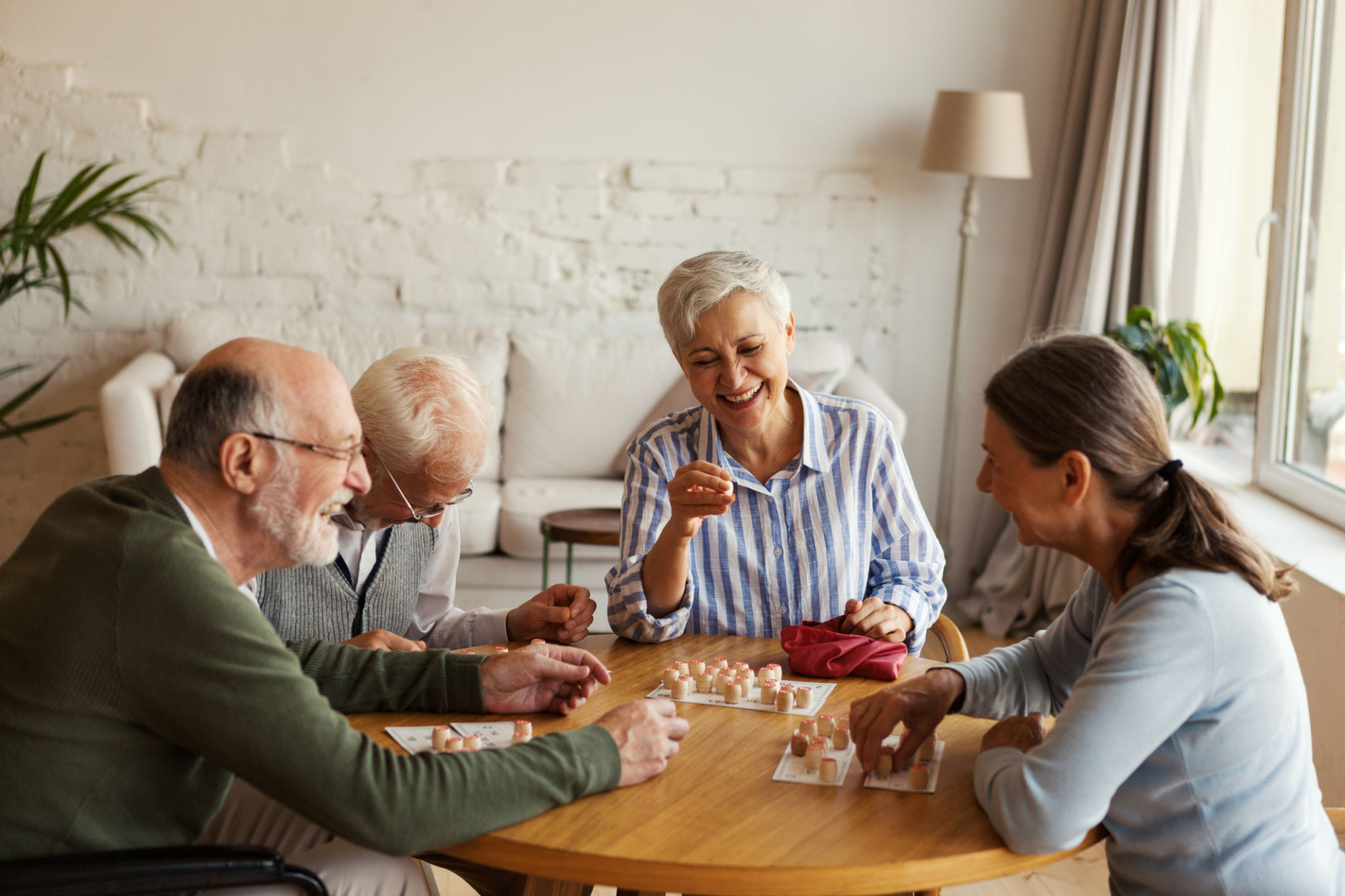 Group of four cheerful senior people, two men and two women, having fun sitting at table and playing bingo game in nursing home Group of four cheerful senior people, two men and two women, having fun sitting at table and playing bingo game in nursing home