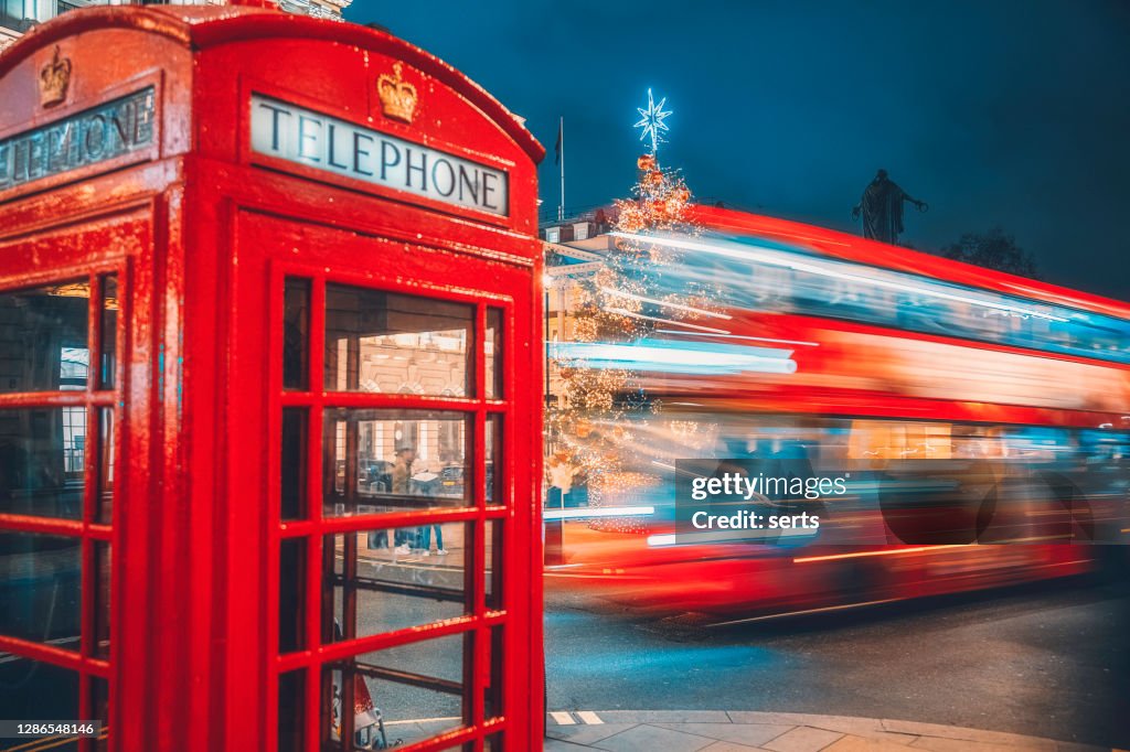 London red telephone booth and speeding double-decker light trails on street at night
