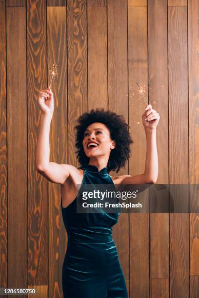 portrait of a young african american woman waving with lit sparklers at a christmas party - christmas party dress stock pictures, royalty-free photos & images