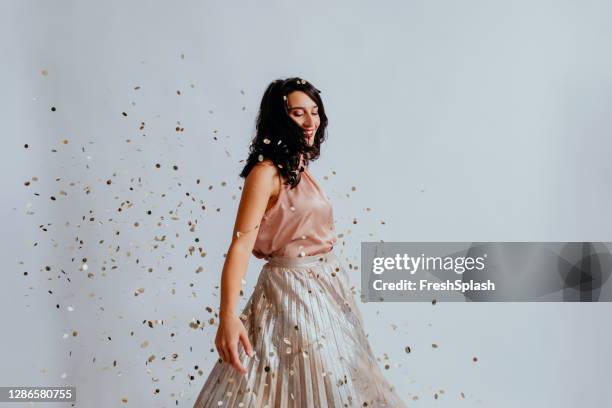 hermosa mujer de pelo negro sonriente bailando bajo confeti en una falda larga y elegante - skirt fotografías e imágenes de stock