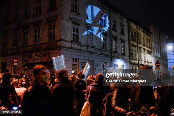 Protesters walk direction to the Main Square while a projection of the National Women's strike logo is screened on a wall during a protest against...