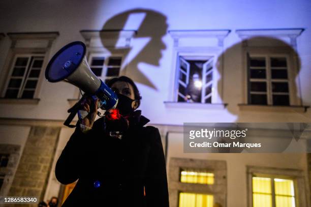 Woman delivers a speech while the National Women's strike logo shape is seen on the Police station wall during a protest against yesterday's police...