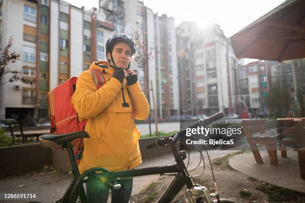 teenage delivery person adjusting cycling helmet while preparing for next delivery - bicycle messenger stock pictures, royalty-free photos & images
