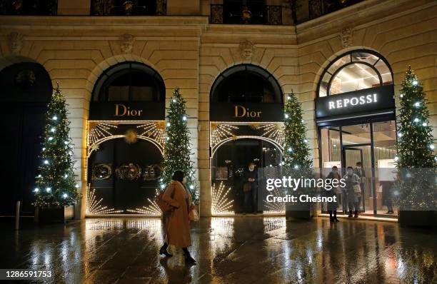 Women wearing protective face masks wait in front of the Dior and Repossi stores on Place Vendome decorated with illuminated Christmas trees for...