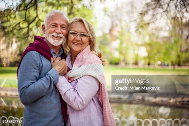 portrait of laughing senior - portrait of a healthy elderly couple standing happy in the park - implante imagens e fotografias de stock