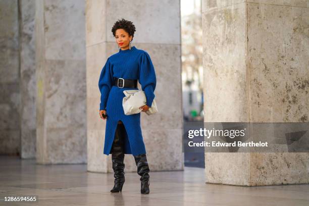 Ellie Delphine wears bejeweled long earrings, a blue oversized knitted wool dress with puff sleeves from Isabel Marant, a white puff leather bag from...