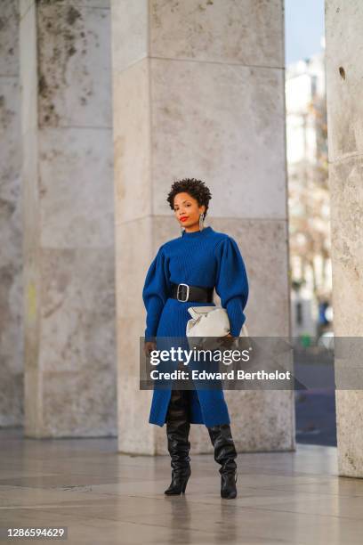 Ellie Delphine wears bejeweled long earrings, a blue oversized knitted wool dress with puff sleeves from Isabel Marant, a white puff leather bag from...