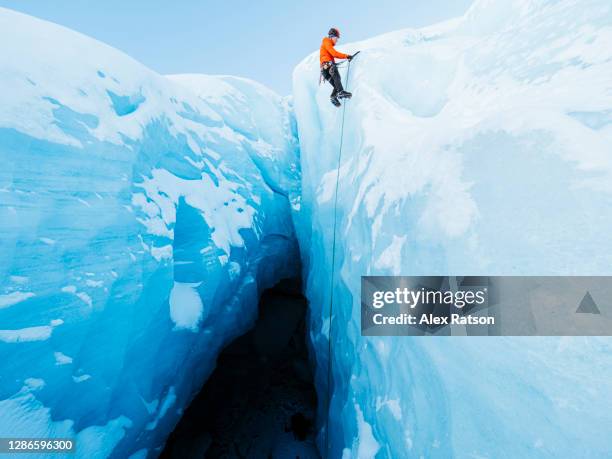 a ice climber at the lip of a tall ice face that drops steeply into a dark ice cave gets ready to be lowered back down. - eisklettern stock-fotos und bilder