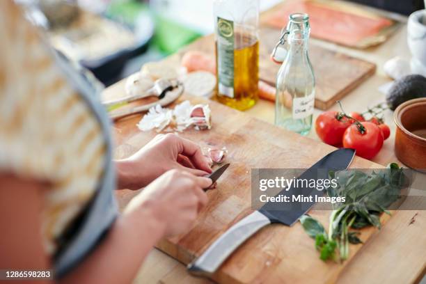 woman in kitchen preparing garlic for cooking on chopping board - chopping vegetables stock pictures, royalty-free photos & images