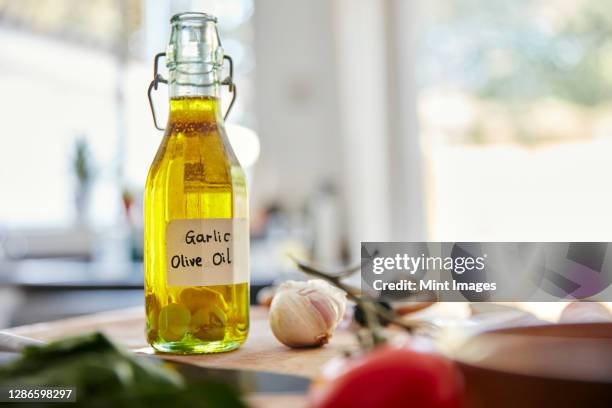 glass bottle contaning olive oil and garlic cloves standing on chopping board in kitchen - chopping garlic stock pictures, royalty-free photos & images