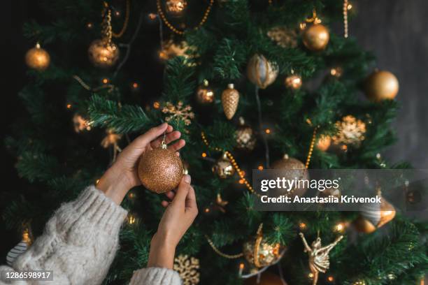 woman putting on christmas tree golden ornaments. - decorar fotografías e imágenes de stock