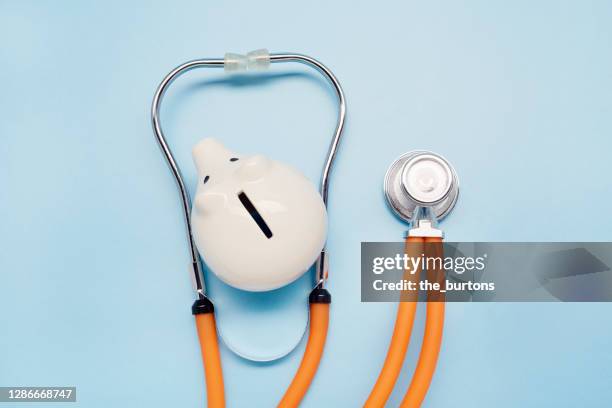 high angle view of stethoscope and piggy bank on blue background - medical insurance stock pictures, royalty-free photos & images