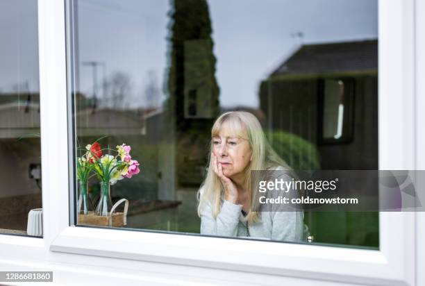 depressed senior woman looking out of window - looking through stock pictures, royalty-free photos & images