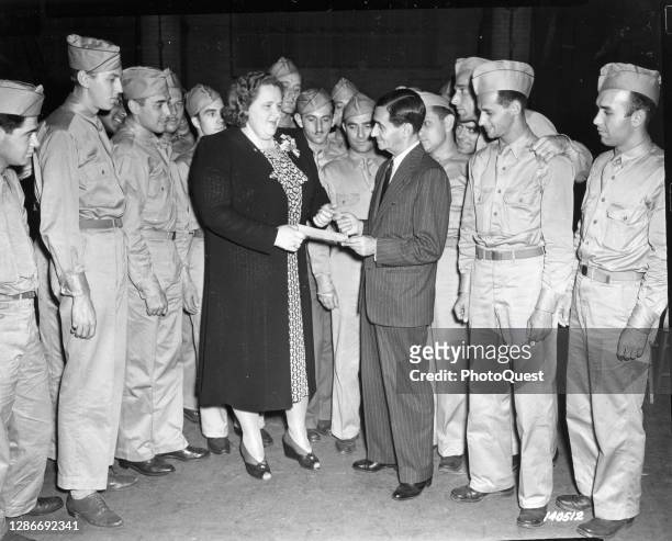 On behalf of the Army Emergency Relief Fund, American singer and radio personality Kate Smith hands a check to composer and musician Irving Berlin in...