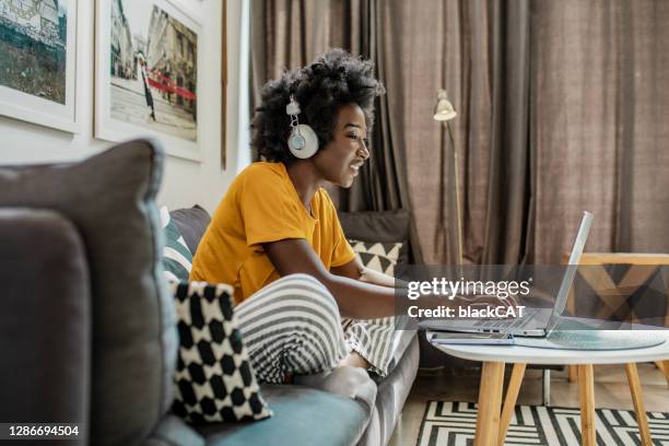 young african american woman with headphones is working from home on laptop - webinars woman stock pictures, royalty-free photos & images