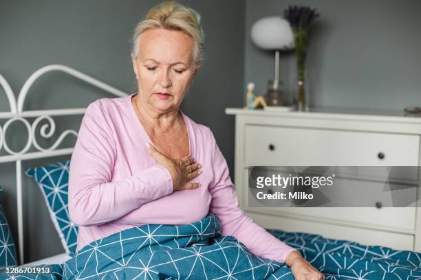 senior woman suffering from chest pain in bed - breathing problems stock pictures, royalty-free photos & images