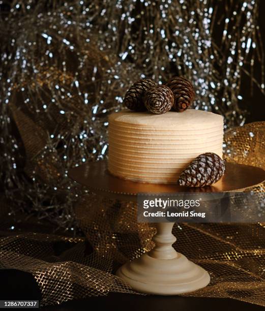 food photography of festive cream front view cake with fir cones on a wooden cake plate on a gold shiny background close up - christmas cake ストックフォトと画像