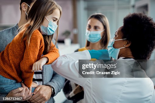 Kleines Mädchen und afroamerikanische Ärztin Ellenbogen stoßen in der medizinischen Klinik. Kleines Mädchen und afroamerikanische Ärztin Ellenbogen stoßen in der medizinischen Klinik.