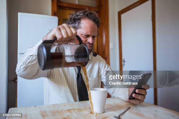 mann, der auf sein handy schaut verschüttet kaffee über den tisch während der arbeit - bloed stock-fotos und bilder