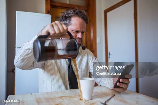 hombre mirando su teléfono móvil derrama café por toda la mesa mientras está en el trabajo - coffee spill fotografías e imágenes de stock