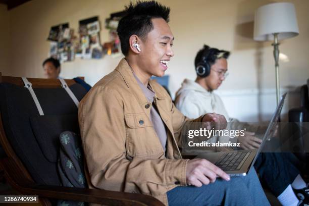 two filipino brothers on laptops in livingroom - in ear headphones stock pictures, royalty-free photos & images