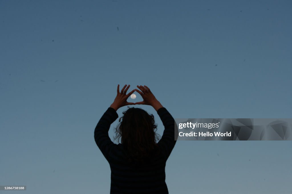 A teenage girl encircles a full moon with her fingers in the crepuscular ight