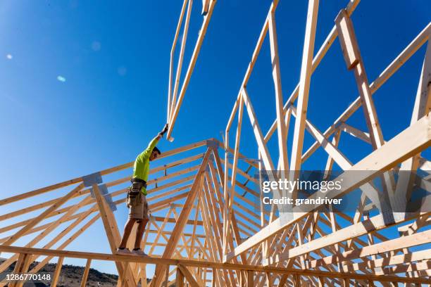 a framer standing on the skelton walls of a new home construction guiding the crane operator to set another truss - lower house stock pictures, royalty-free photos & images