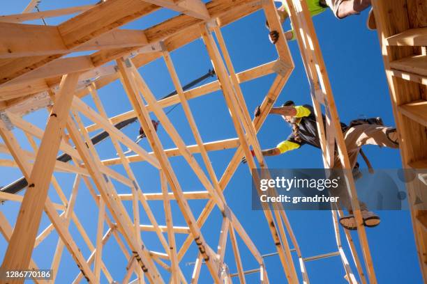 a framer standing on the skelton walls of a new home construction guiding the crane operator to set another truss - roof truss stock pictures, royalty-free photos & images